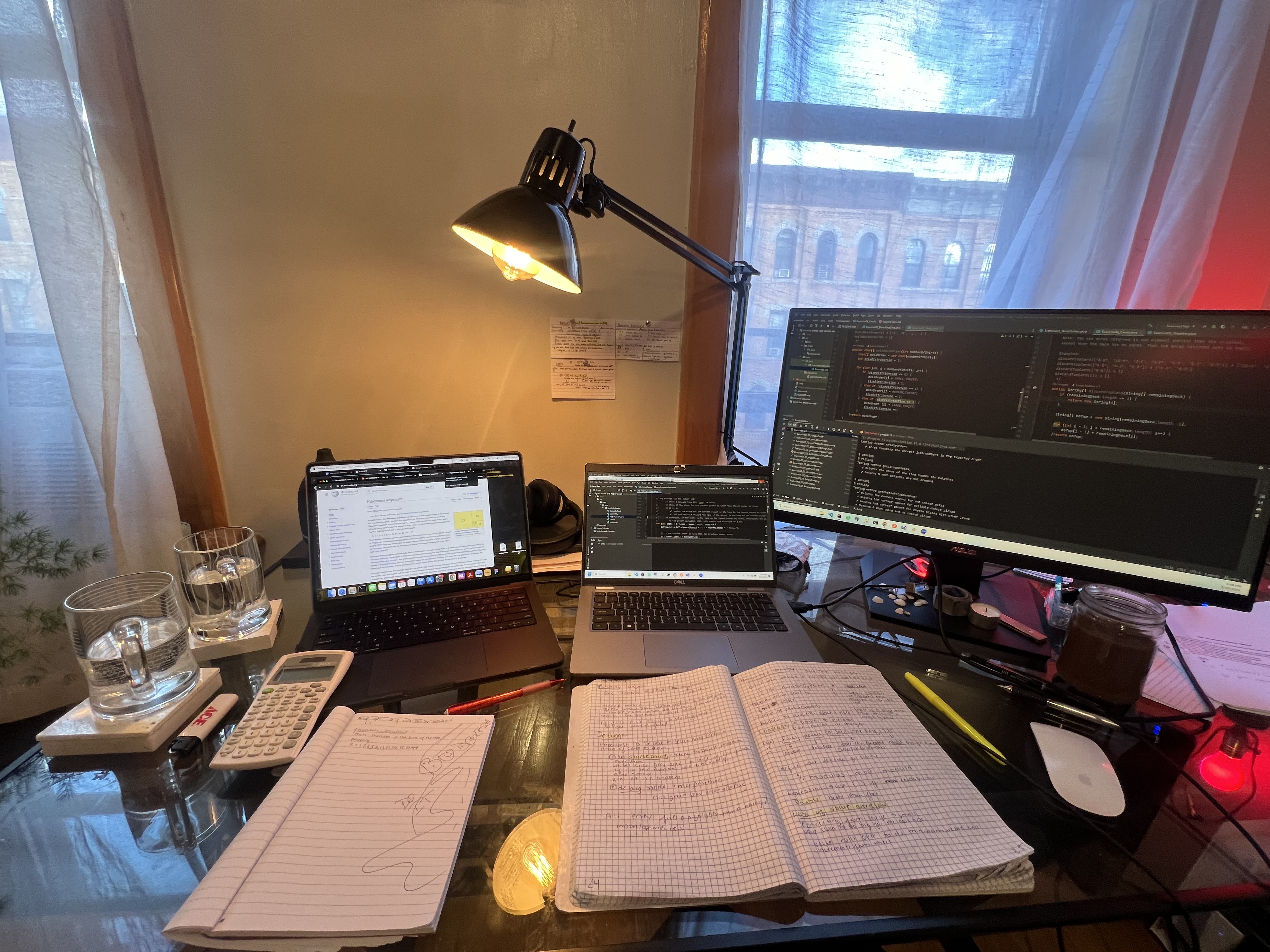 Coding desk with laptop, monitor, notebooks, and Java code open in the IDE.